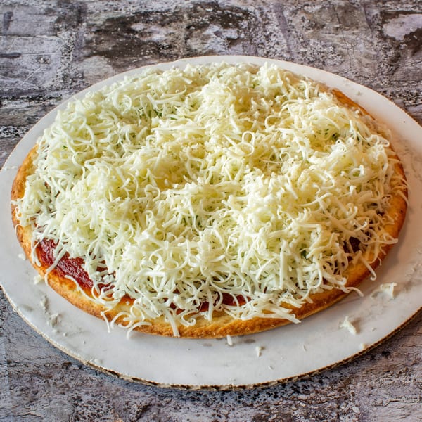 Uncooked Stavro's Pizza House IV pizza with a thick layer of shredded mozzarella cheese.