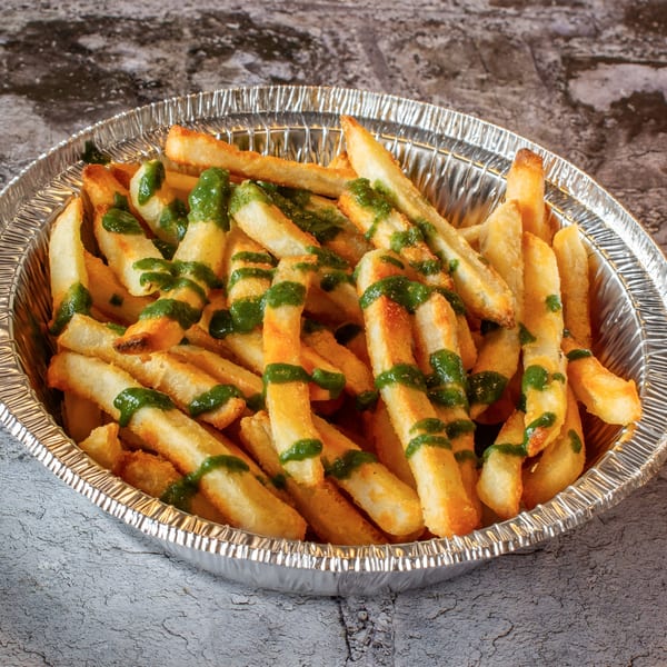 Golden french fries drizzled with green pesto sauce in a silver foil container.
